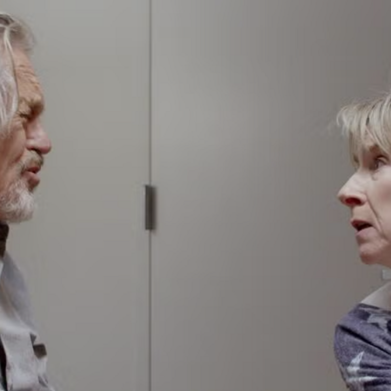 Miles Anderson and Bella Merlin staring at each other in conversation with an office background