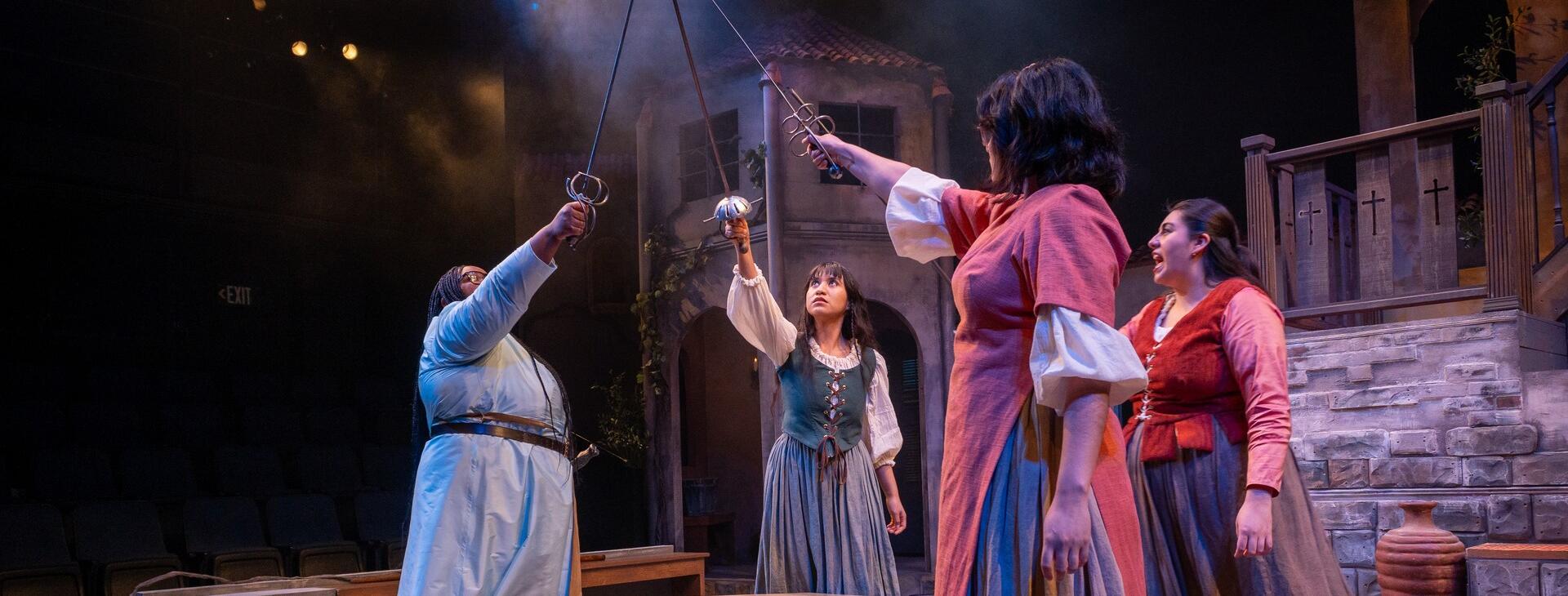 Four women on stage in costumes raising swords